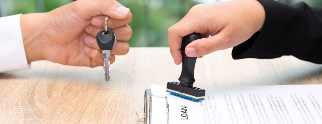 One hand stamping a loan application form and another hand handing over the keys